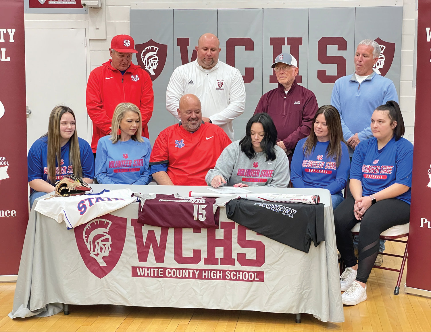 Family members, coaches, and college representatives gather around Ashlynn Phillips as she signs her Letter of Intent.
